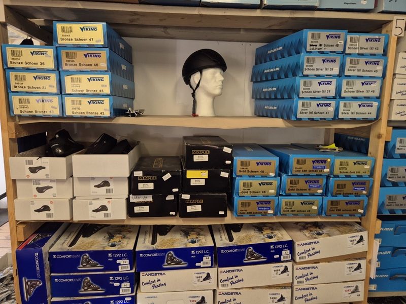 Kast in de winkel vol dozen met nieuwe schaatsen en een schaatshelm